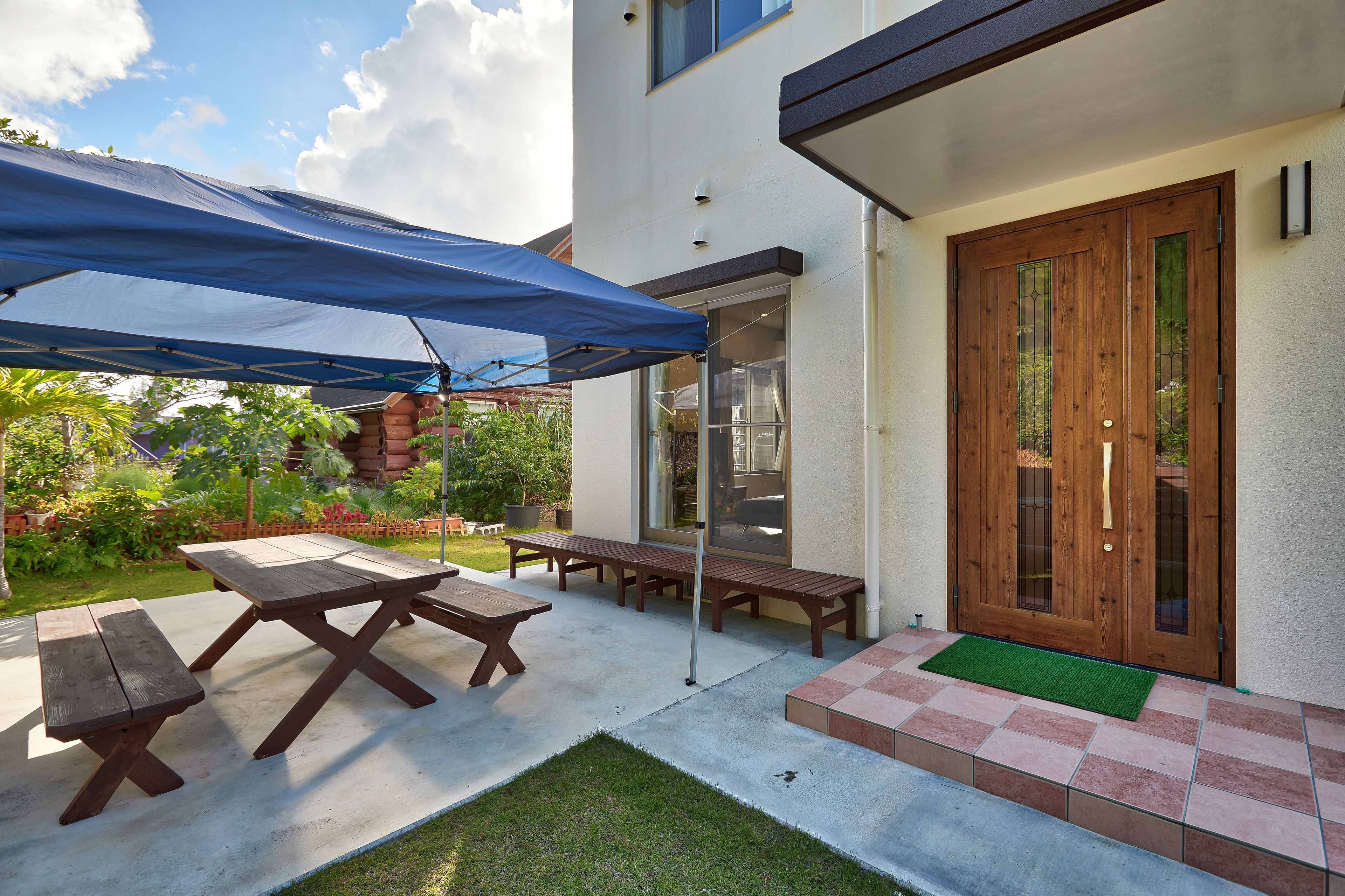 A patio area with picnic tables, a blue canopy, and a wooden door.