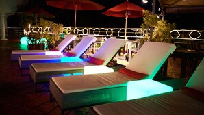 Outdoor lounge chairs with red umbrellas, illuminated by colorful lights. - The Pool Resort Villa Hasta Manana (Onna)