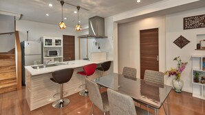 A modern kitchen with a central island, bar stools, and a dining table. - The Pool Resort Villa Hasta Manana (Onna)