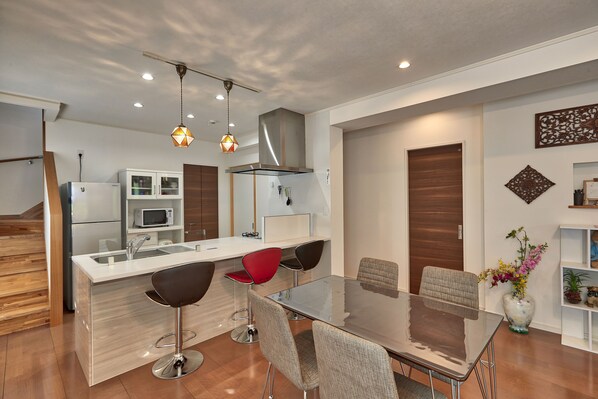 A modern kitchen with a central island, bar stools, and a dining table. - The Pool Resort Villa Hasta Manana (Onna)
