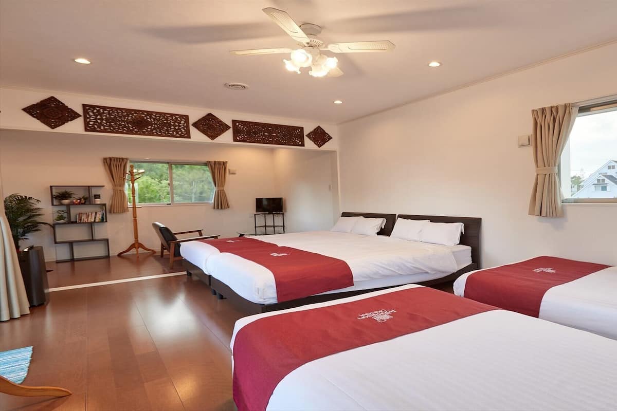 A hotel room with two beds, a TV, a bookshelf, and a window with curtains.