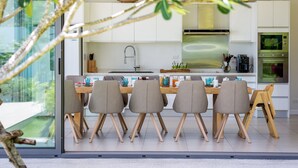 Une cuisine moderne avec un coin repas, comprenant un grand îlot central, des meubles blancs et une vue dégagée grâce à des portes vitrées.