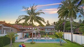Une maison moderne dotée d’une piscine, de palmiers et d’une pelouse bien entretenue.