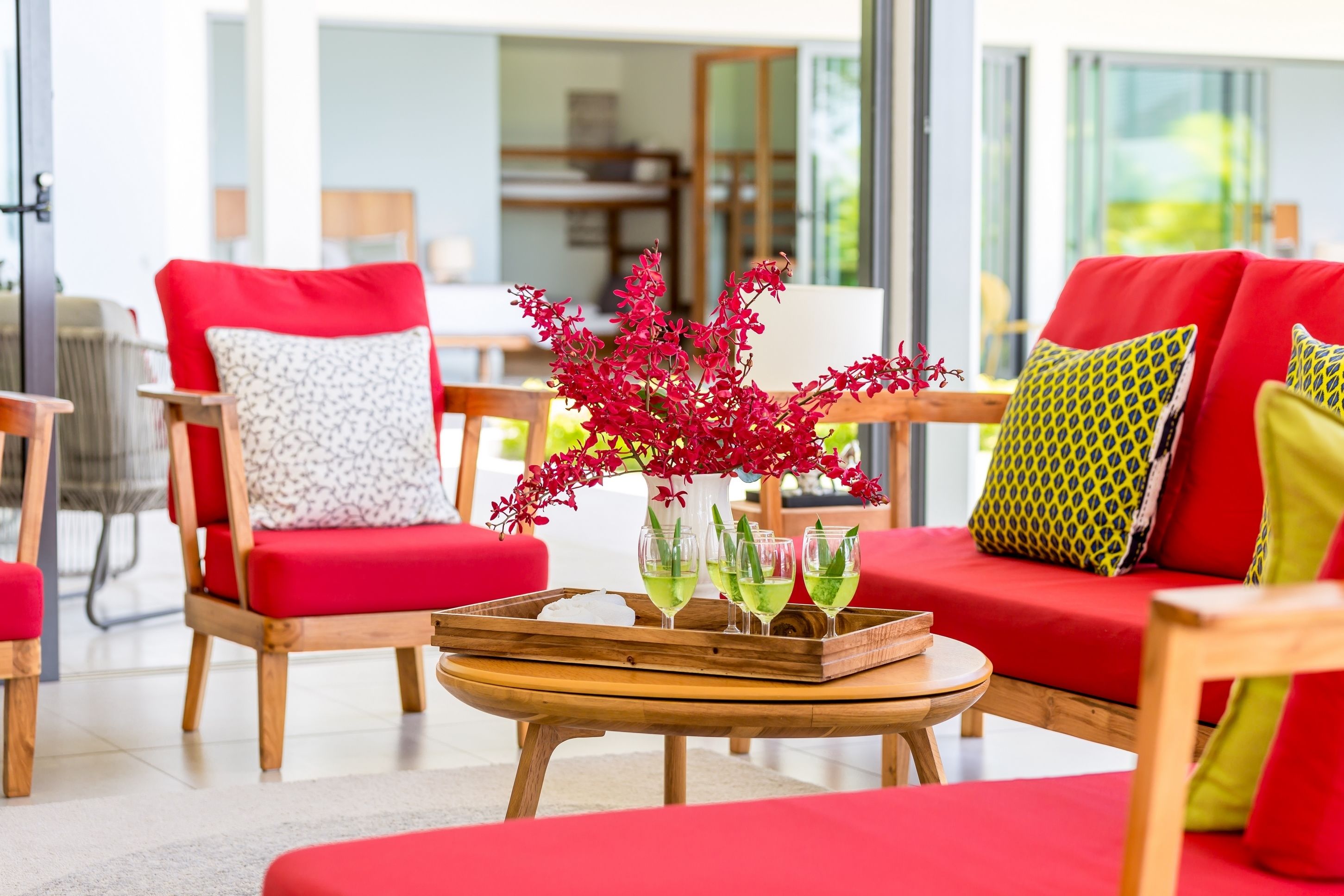 A modern living room with red sofas, wooden chairs, and a coffee table with a tray of drinks and a red plant.
