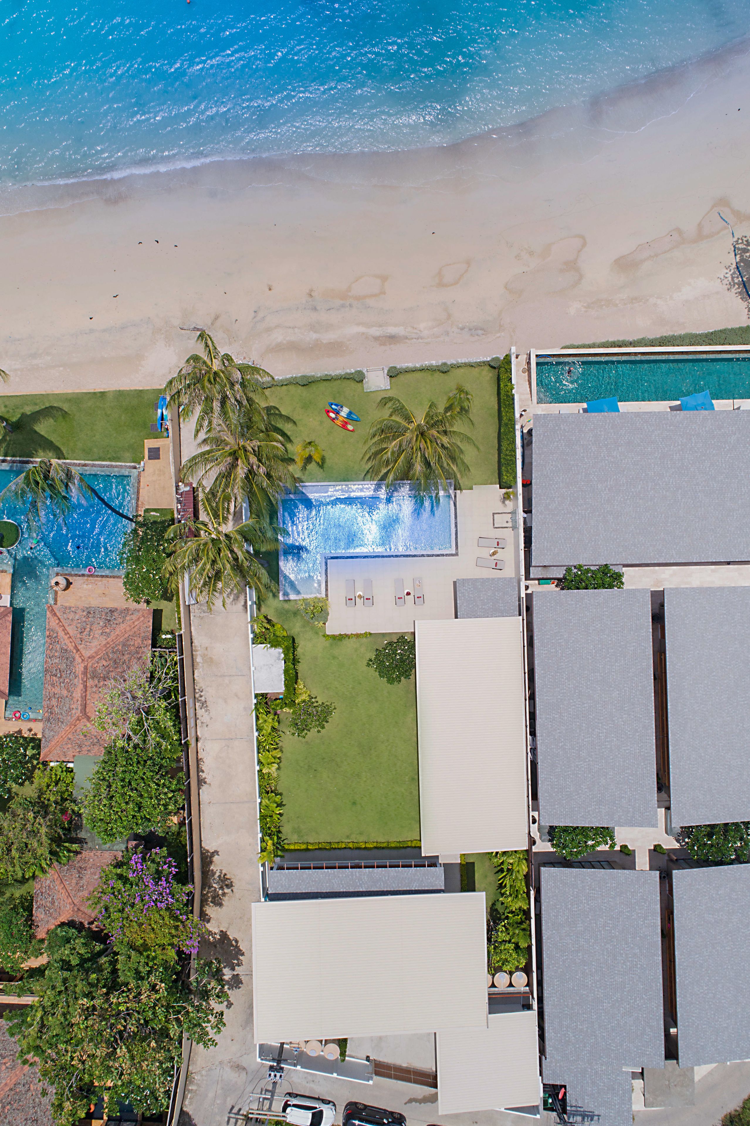 An aerial view of a resort with a swimming pool, beach, and palm trees.