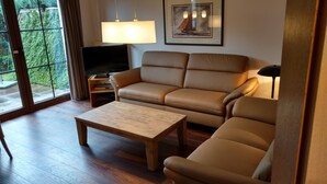 A living room with a sofa, a coffee table, a TV, and a painting on the wall. - Holiday house, WiFi, close to the beach, max. 6 people, 80sqm, 3 bedrooms, barbecue area  (Butjadingen)