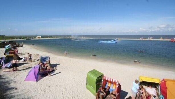 A beach with people relaxing under colorful umbrellas, a clear blue sky, and a calm sea. - Holiday house, WiFi, close to the beach, max. 6 people, 80sqm, 3 bedrooms, barbecue area  (Butjadingen)