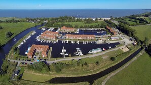 Vista aérea de un puerto deportivo con varios muelles, barcos y un edificio grande con tejados rojos.