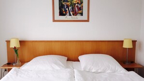 Habitación de hotel con cabecera de madera, dos mesitas de noche con lámparas y una obra de arte enmarcada sobre la cama.
