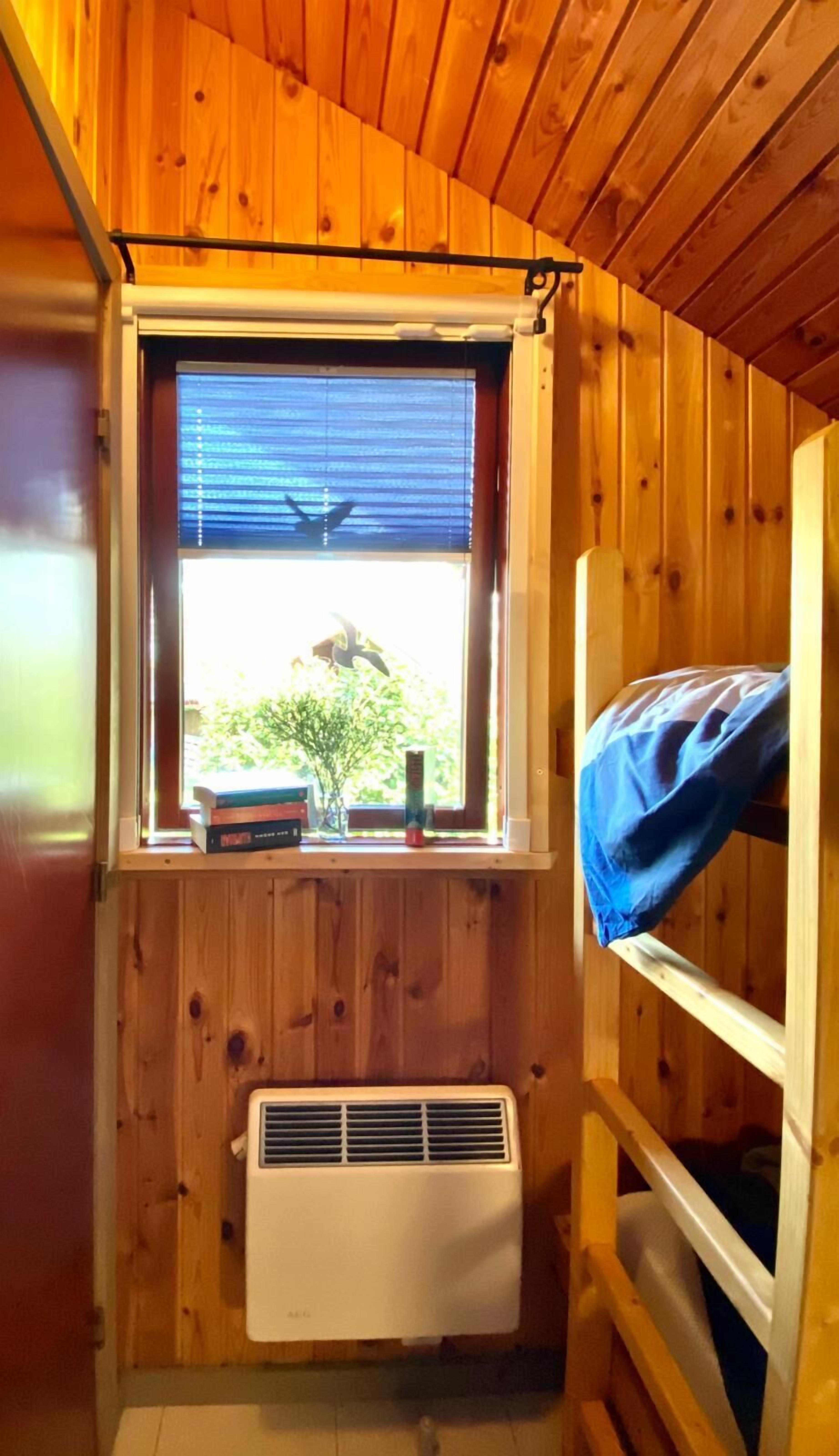 Eine kleine Holzhütte mit Fenster, Heizkörper und Etagenbett.