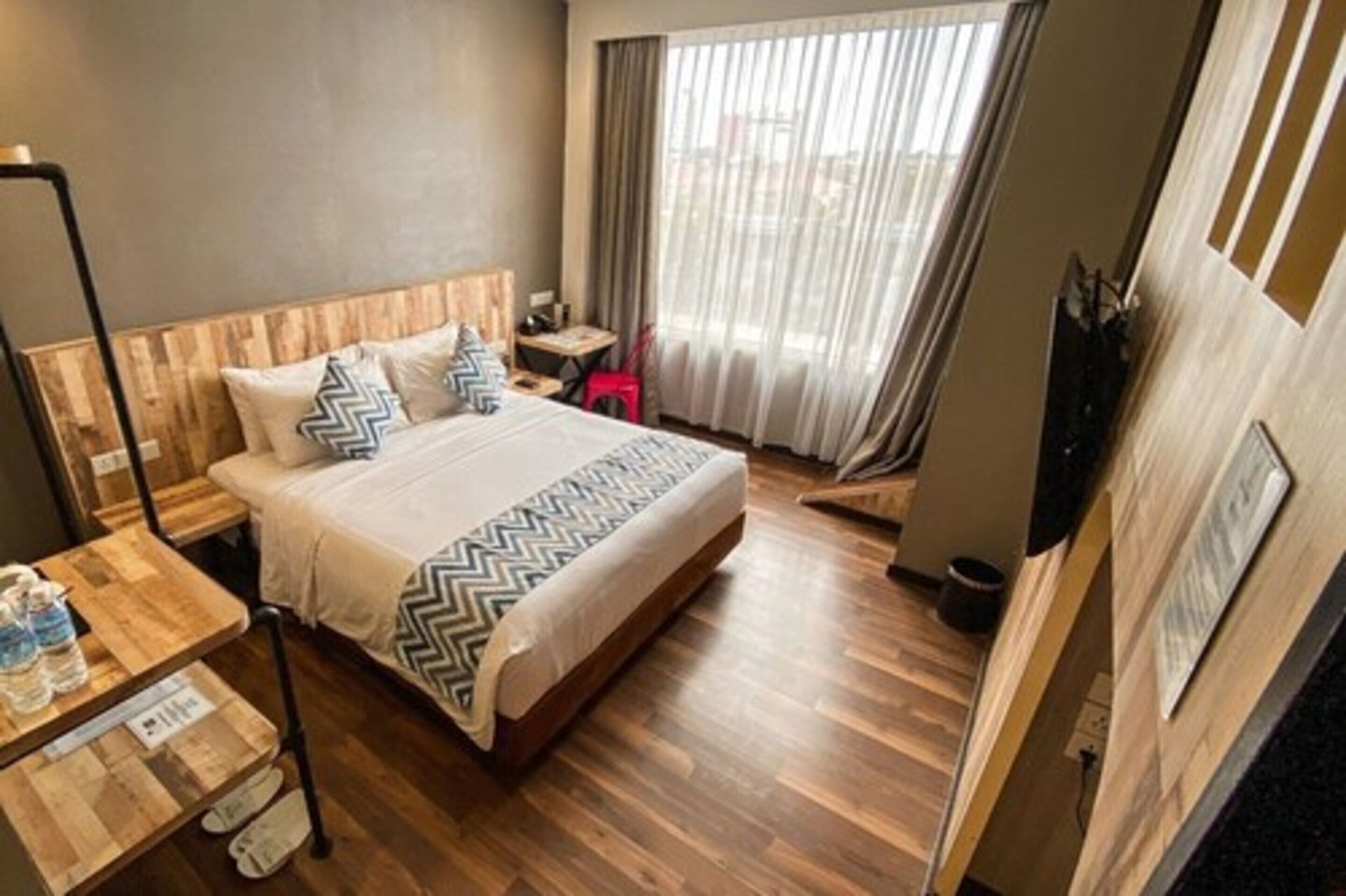A hotel room with a wooden bed, a small table with a water bottle, a chair, and a TV on the wall.