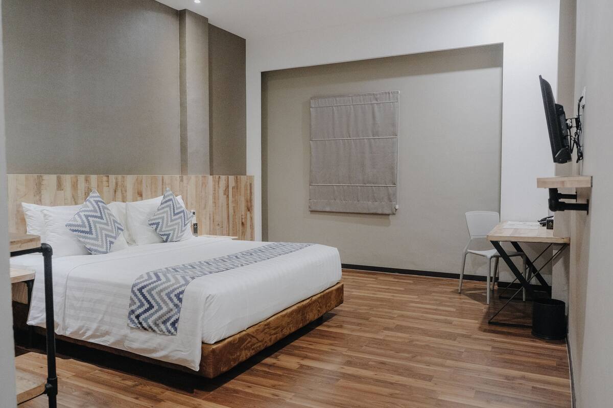 Une chambre moderne avec une tête de lit en bois, un lit avec une literie à motifs, un bureau avec une chaise et une fenêtre avec un rideau.