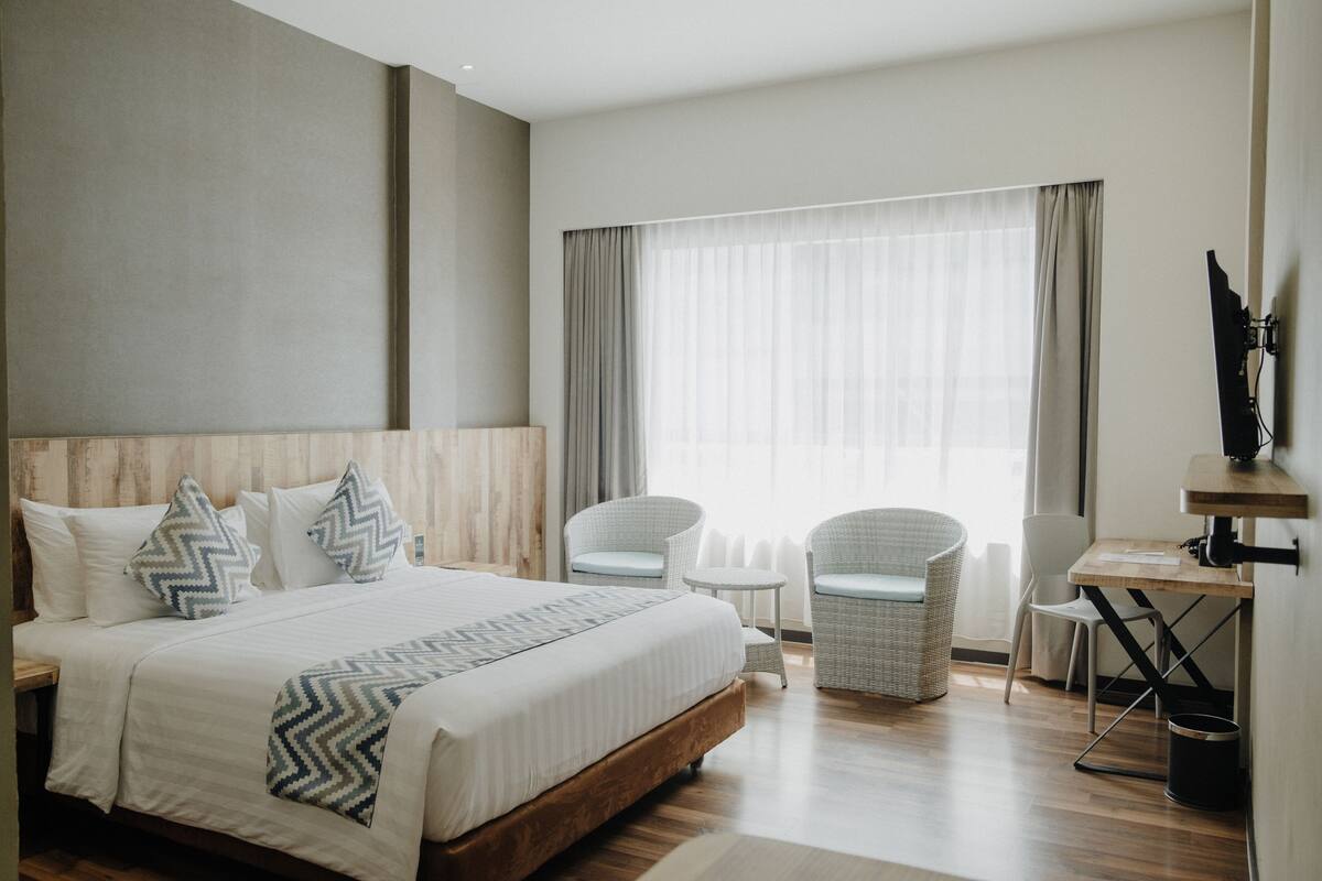 Une chambre d’hôtel moderne avec un grand lit, deux fauteuils, une petite table et un bureau.