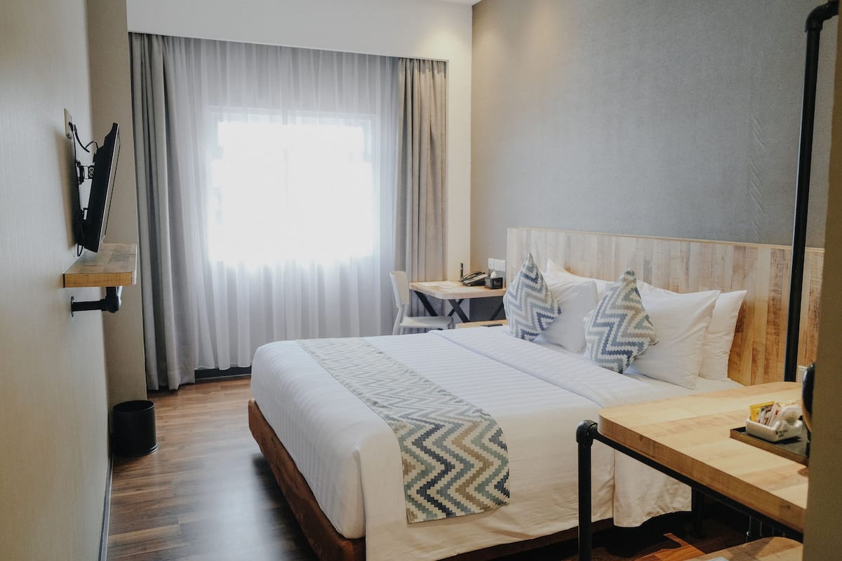 Une chambre d’hôtel avec un lit, un bureau, une chaise et une fenêtre avec des rideaux.