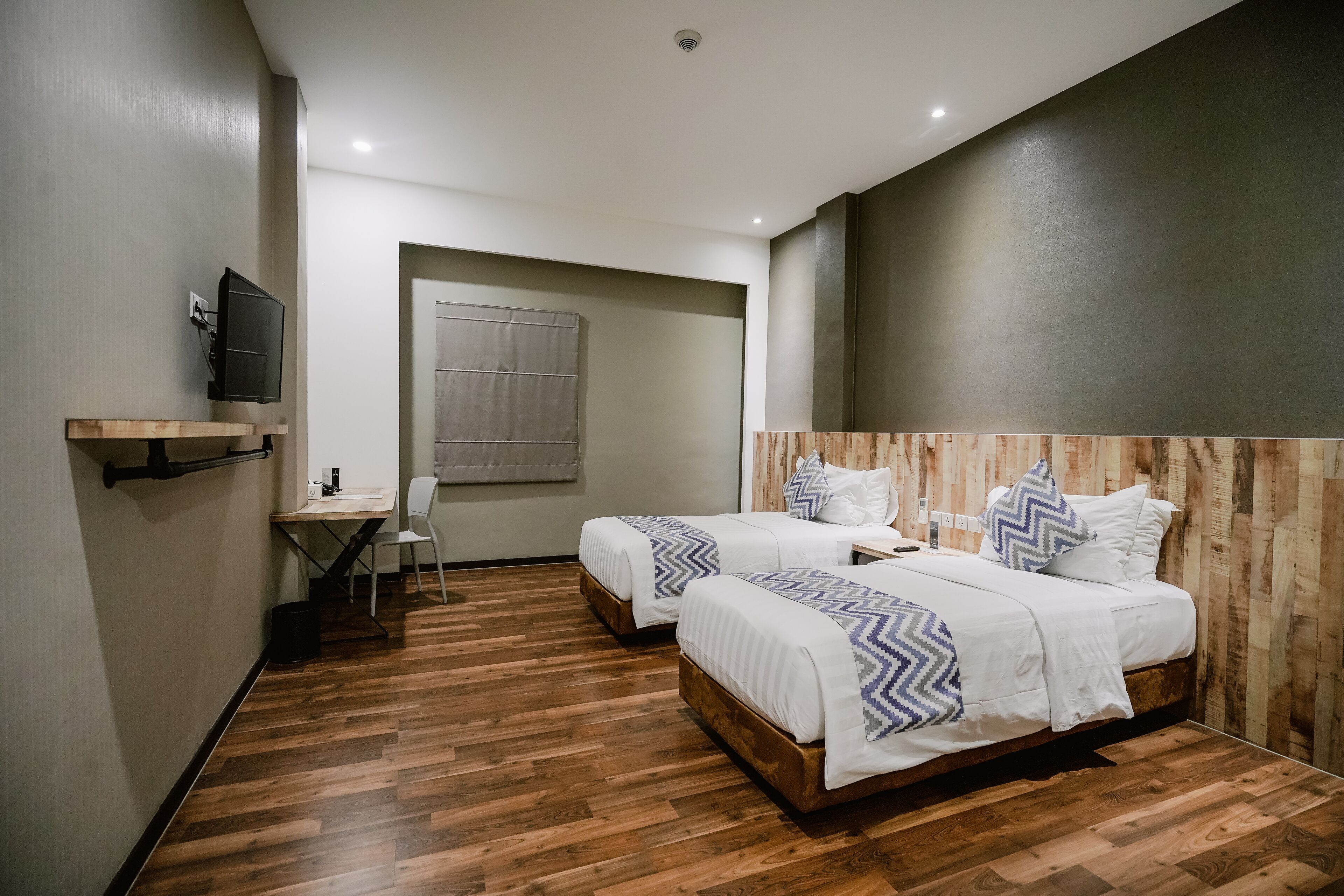 A modern hotel room with two beds, a desk, and a television.