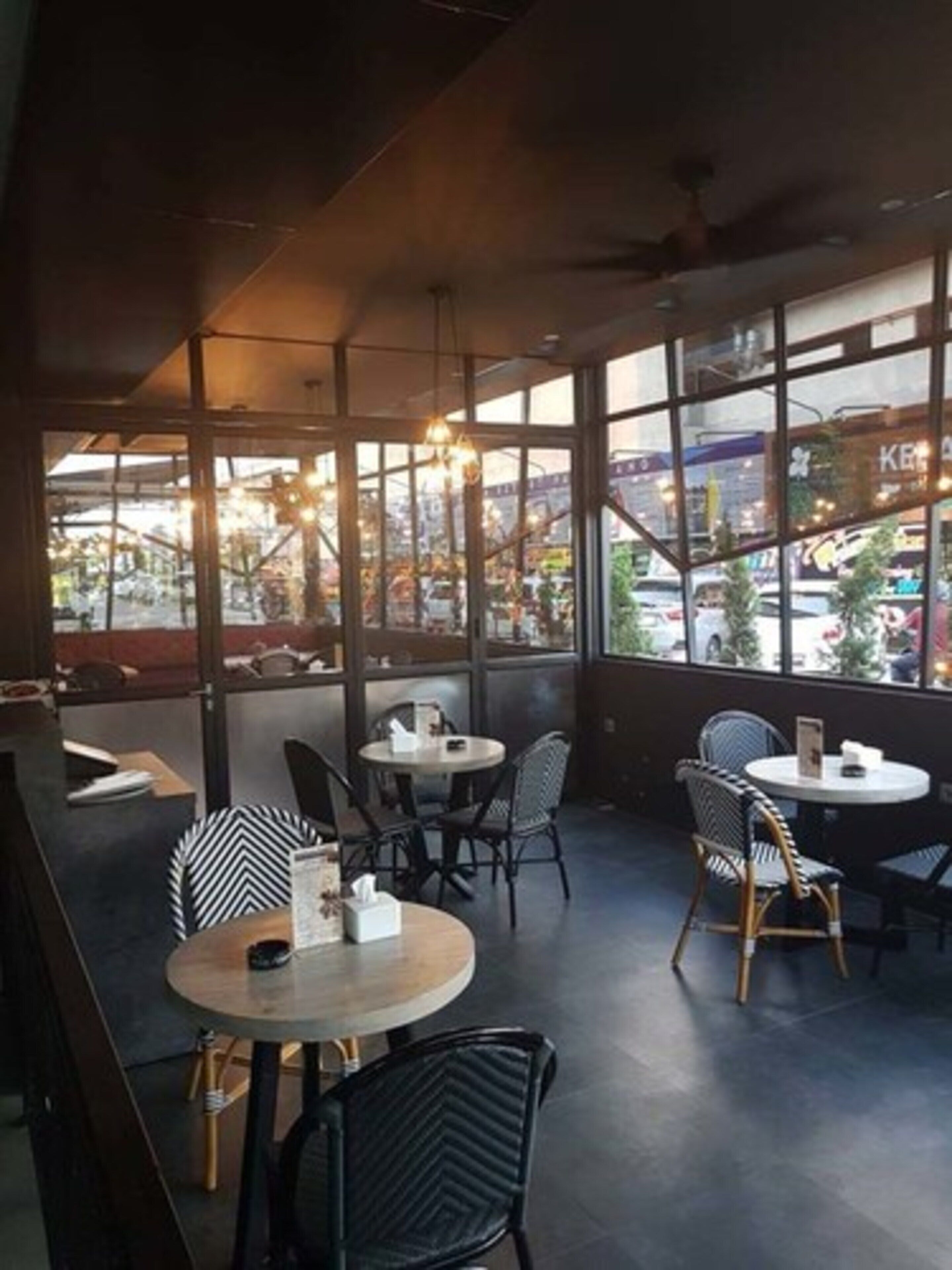 A modern restaurant with round tables and black and white patterned chairs, large windows offering views of a cityscape and a bridge.