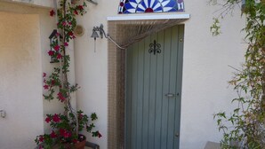 A green door with a decorative metal emblem, a small bell, and a wall-mounted light fixture. - Studio meublé de vacances, very quiet in nature and culture ancient and modern (Sanilhac-Sagriès)