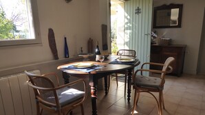 A dining area with a table set for two, surrounded by wicker chairs, a wooden cabinet, and a mirror on the wall. - Studio meublé de vacances, very quiet in nature and culture ancient and modern (Sanilhac-Sagriès)