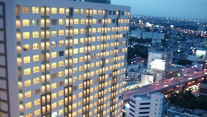 Un edificio alto con numerosas ventanas, presumiblemente un hotel, rodeado de otros edificios y una calle concurrida con vehículos en movimiento.