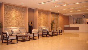 Un moderno vestíbulo de hotel con mostrador de recepción, zona de estar con sofás y sillones, y una pared decorativa con diseño de mosaico.