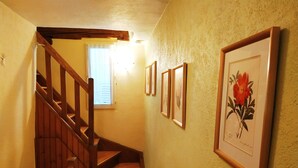 Eine Holztreppe mit Handlauf, ein Fenster mit weißen Vorhängen und gerahmte Pflanzenbilder an der Wand.