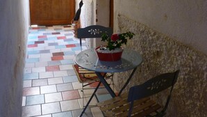 Ein schmaler Korridor mit gefliestem Boden, einer Holztür am Ende sowie einem kleinen Tisch mit Stühlen und einem Blumentopf.