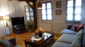 Ein Wohnzimmer mit einer Sofagarnitur, einem Couchtisch mit Blumenarrangement, einem Fernseher und einer Lampe.
