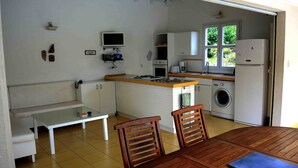 A compact kitchen with a dining area, including a table, chairs, a bench, and a washing machine.
