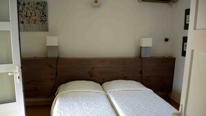 A room with a wooden headboard, two beds with white linens, a wall-mounted air conditioner, and a poster on the wall.