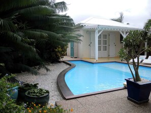 Uma piscina de borda curva, rodeada por uma área de cascalho e plantas em vasos.