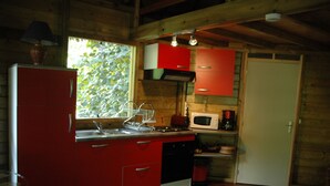 A compact kitchen with red cabinets, a microwave, a sink, and a window with a view of greenery. - My cabin-Star Trail (POINTE NOIRE)