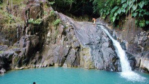 A natural hot spring with clear turquoise water surrounded by rocky terrain and lush greenery. - My cabin-Star Trail (POINTE NOIRE)