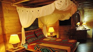 A wooden cabin-style room with a four-poster bed, two bedside lamps, and a mirror on the wall. - My cabin-Star Trail (POINTE NOIRE)