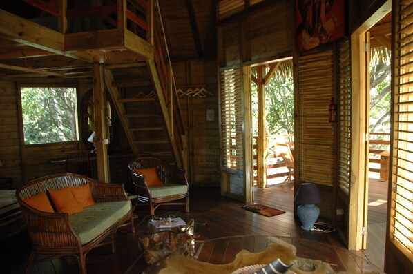 A wooden cabin interior with a staircase, wicker furniture, and a glass coffee table.