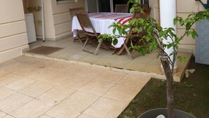 A covered patio area with a table set for dining, a small tree, and a potted plant with rocks. - Ermitage Les Bains - Apt F2 - Ground floor - Lagoon proximity (SAINT GILLES LES BAINS)