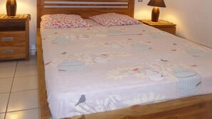 A neatly made bed with a floral bedspread, two bedside lamps, and a wooden headboard. - Ermitage Les Bains - Apt F2 - Ground floor - Lagoon proximity (SAINT GILLES LES BAINS)