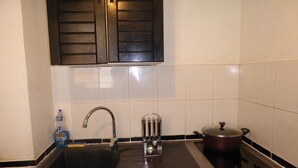 A kitchen with a black sink, stainless steel faucet, a pot on the stove, and a bottle of dish soap. - Ermitage Les Bains - Apt F2 - Ground floor - Lagoon proximity (SAINT GILLES LES BAINS)