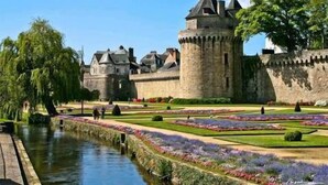 Un castell històric amb fossat, envoltat de jardins cuidats i un cel serè.