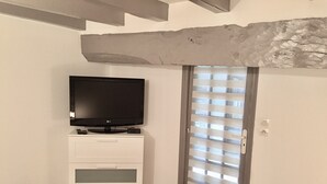 Un dormitori amb una televisió sobre un taulell blanc, una porta amb persianes i un biga de pedra sobre la porta.