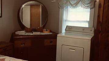 Un dormitorio con cama, cómoda, espejo, ventana y lavadora.