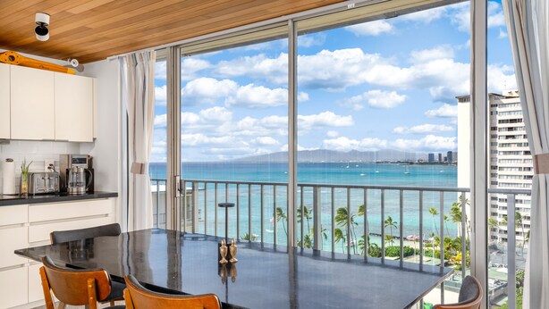 A modern kitchen with white cabinets, a black countertop, and a view of the ocean through large glass doors. - True Top Floor Penthouse Residence with 360 Degree Views & A/C (Honolulu)