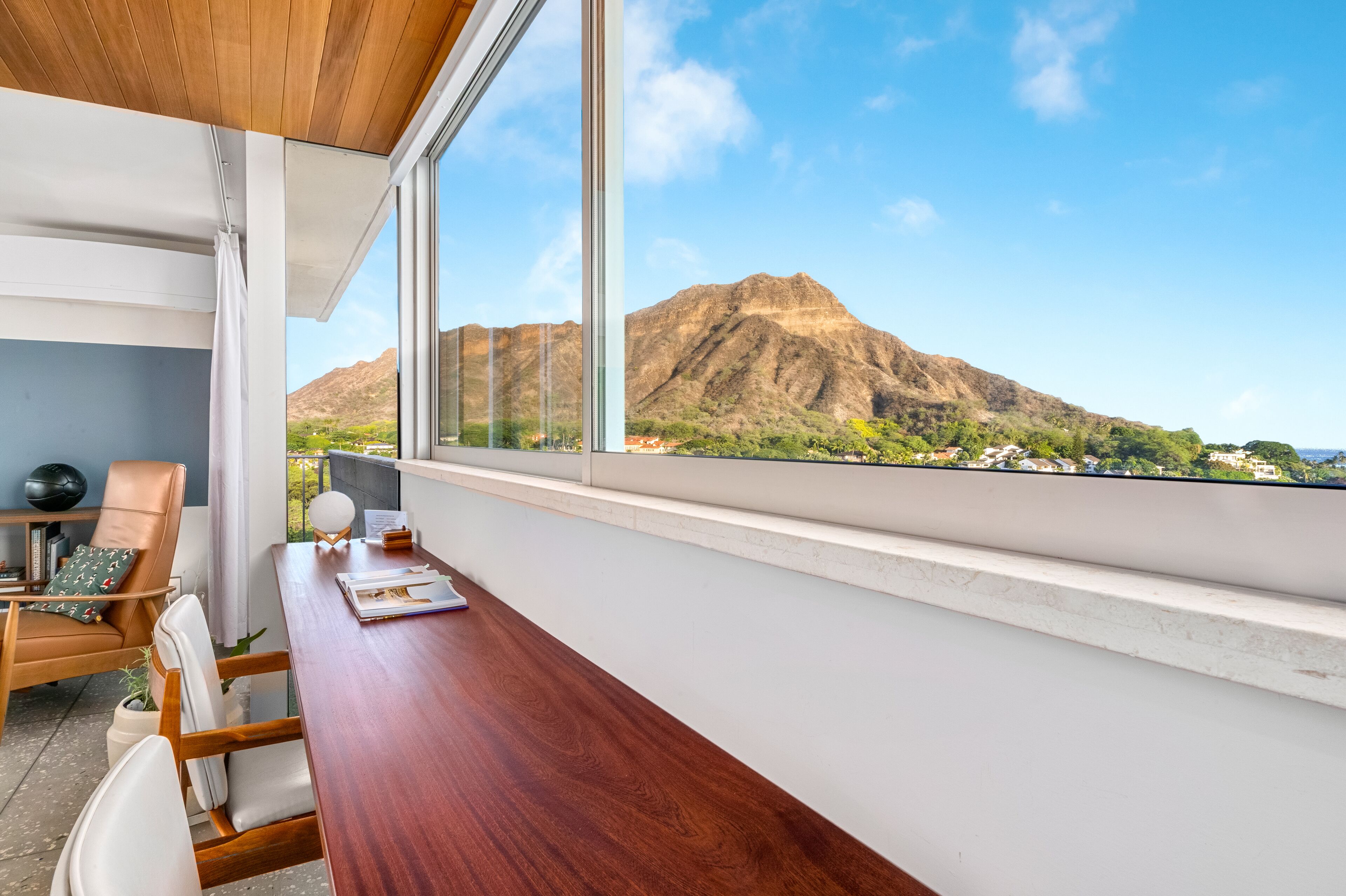 A modern room with a wooden desk, white chairs, and a large window offering a view of mountains.