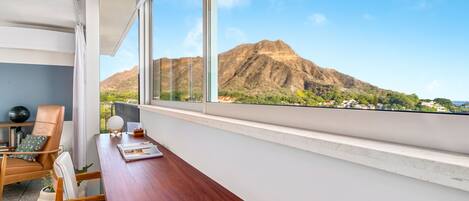 A modern room with a wooden desk, white chairs, and a large window offering a view of mountains.