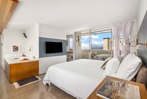 Quarto de hotel moderno com cama grande, televisão na parede, banheiro com pia e espelho, e varanda com vista para a cidade.