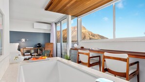 A modern room with a large window, a desk, two chairs, a small table, and a bathtub. - True Top Floor Penthouse Residence with 360 Degree Views & A/C (Honolulu)