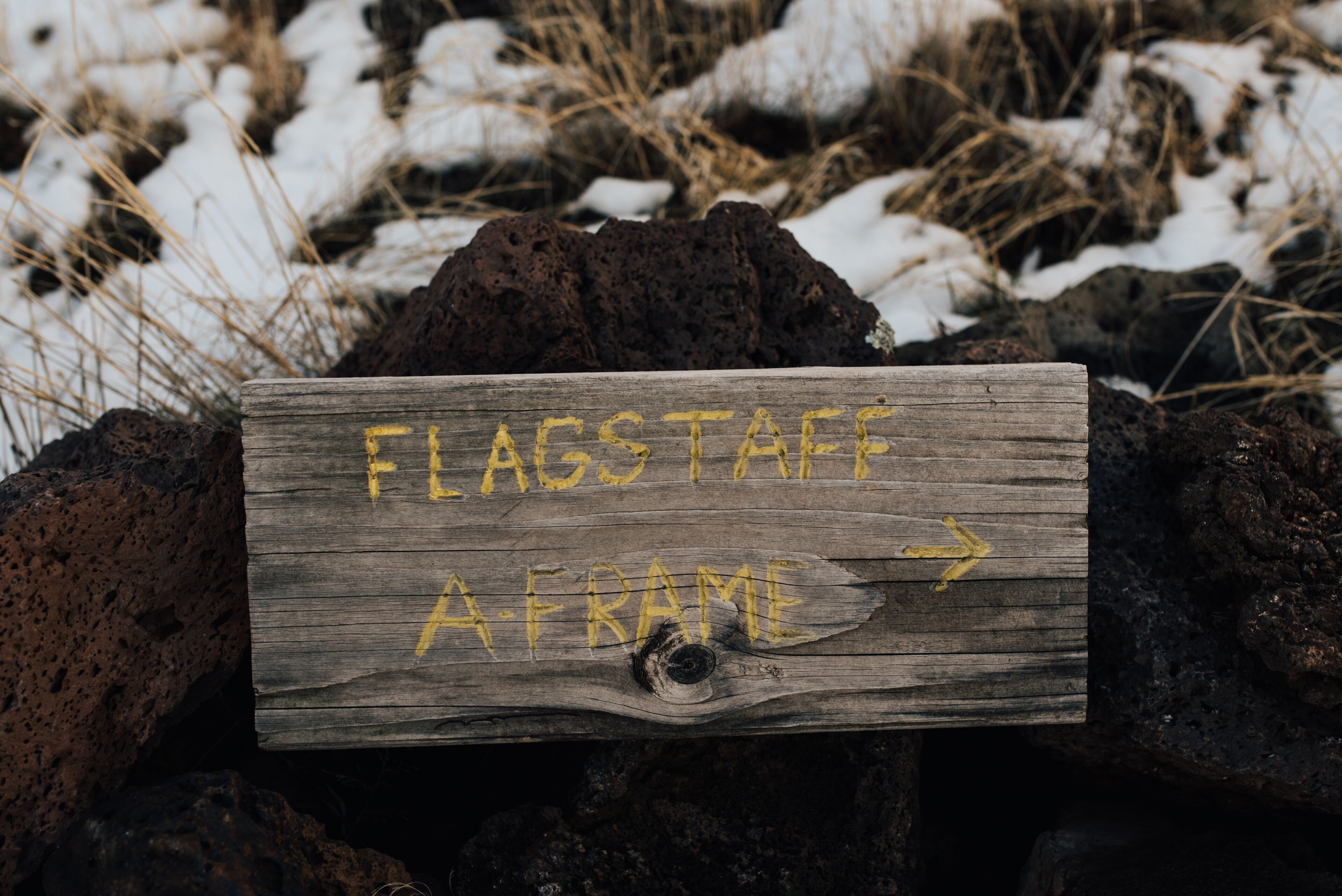 A wooden sign with yellow text reading "FLAGSTAFF A FRAME" and an arrow pointing right.