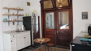 Una cocina compacta con armarios blancos, un refrigerador de acero inoxidable, una mesa de madera con cuatro sillas y un par de puertas con un espejo.