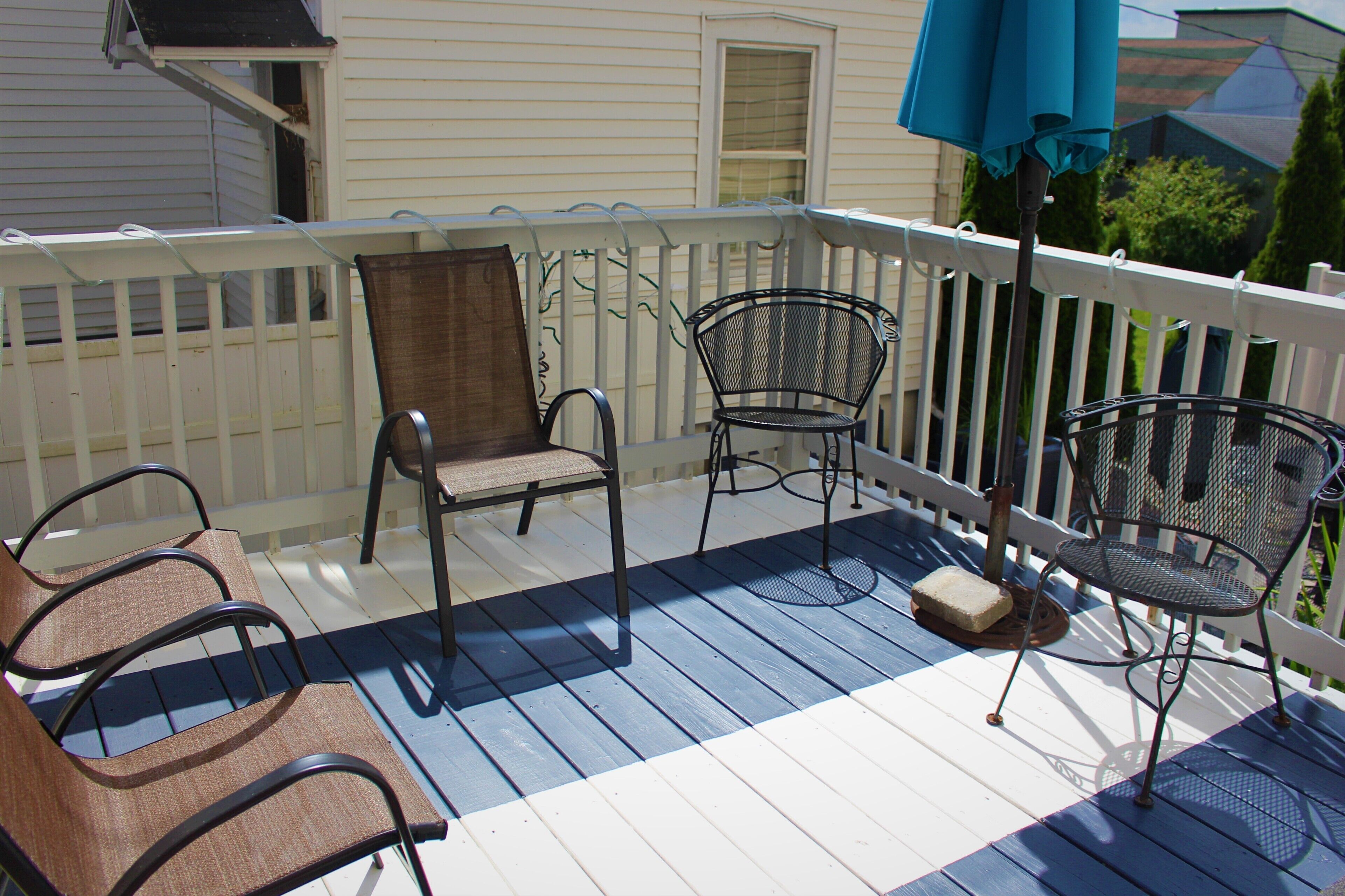 A covered outdoor deck with a white railing, two metal chairs, and a blue umbrella.