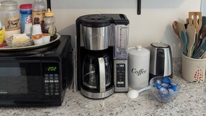 Una cocina con cafetera, microondas y diversos utensilios de cocina sobre la encimera.