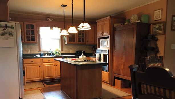 Una cocina con armarios de madera, una isla central, luces colgantes y un refrigerador, además de un microondas.
